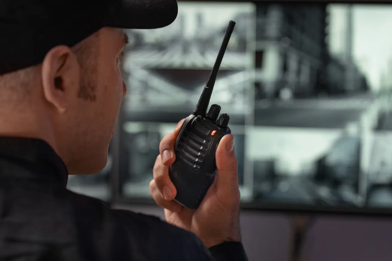 Porteiro com rádio comunicador acompanhando monitores na guarita