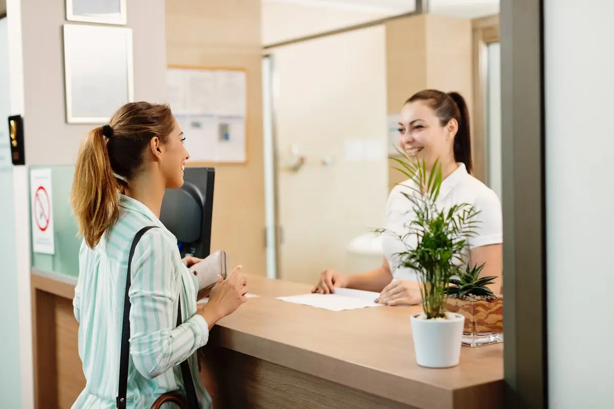 Recepcionista atendendo visitante no balcão de entrada de uma empresa